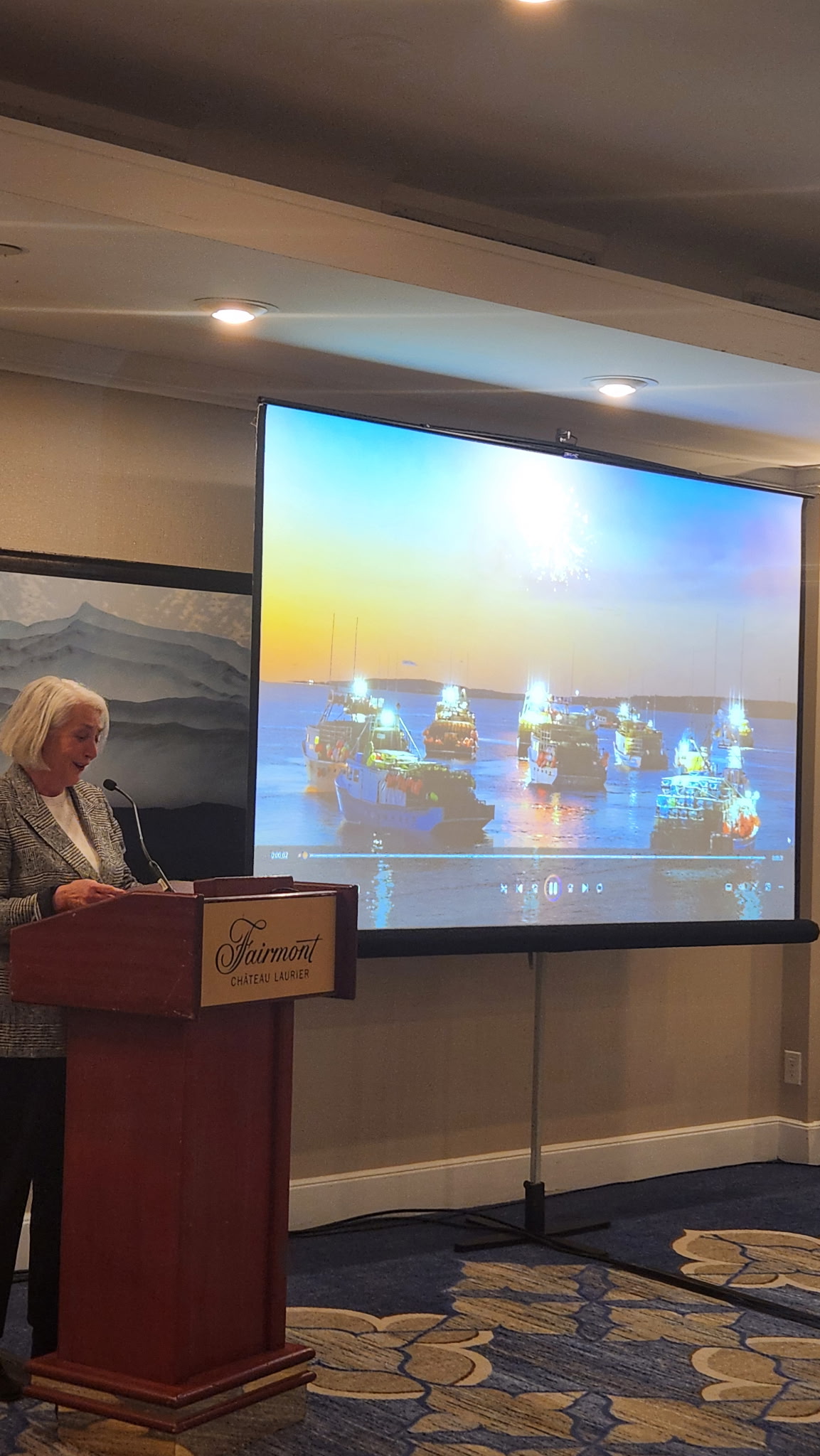 Federation speaker addressing the room, with a screen behind showing a fleet of fishing boats lit up at dusk
