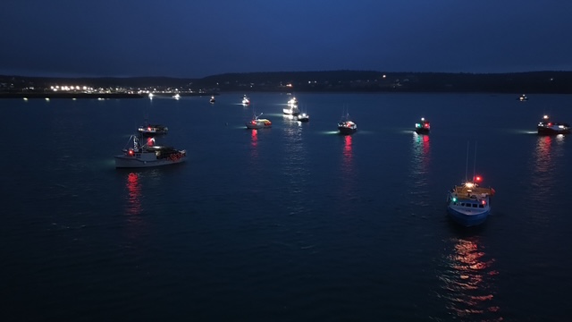 Fishing fleet heading out at dawn, aerial drone view of boats with navigation lights scattered across the bay
